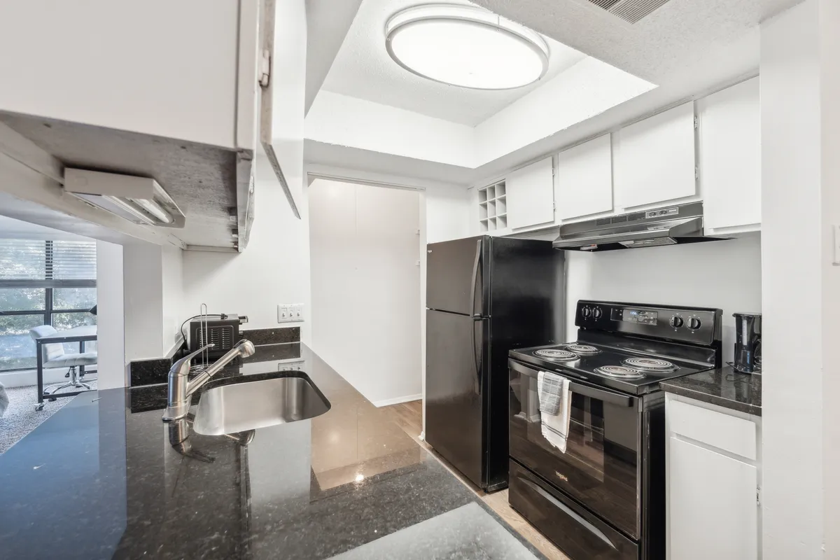 This image showcases a modern kitchen with sleek black appliances, granite countertops, and crisp white cabinetry. The layout is open and functional, with clean lines and abundant counter space ideal for meal prep and socializing.
