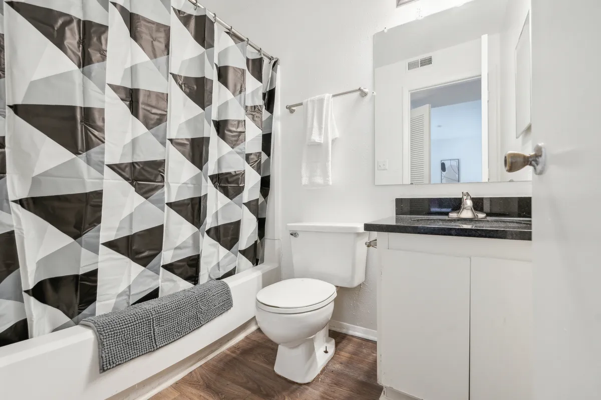 A modern bathroom featuring a geometric shower curtain, sleek black countertop, and updated fixtures. The atmosphere is functional and contemporary, perfect for moments of self-care or shared routines.
