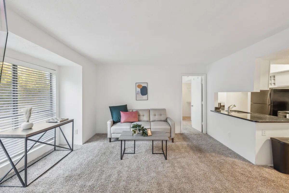 This cozy, modern living area is filled with natural light streaming through the window and is furnished with a comfortable sofa, coffee table, and stylish artwork. The setup suggests a space ideal for relaxing, reading, or socializing after a productive day.