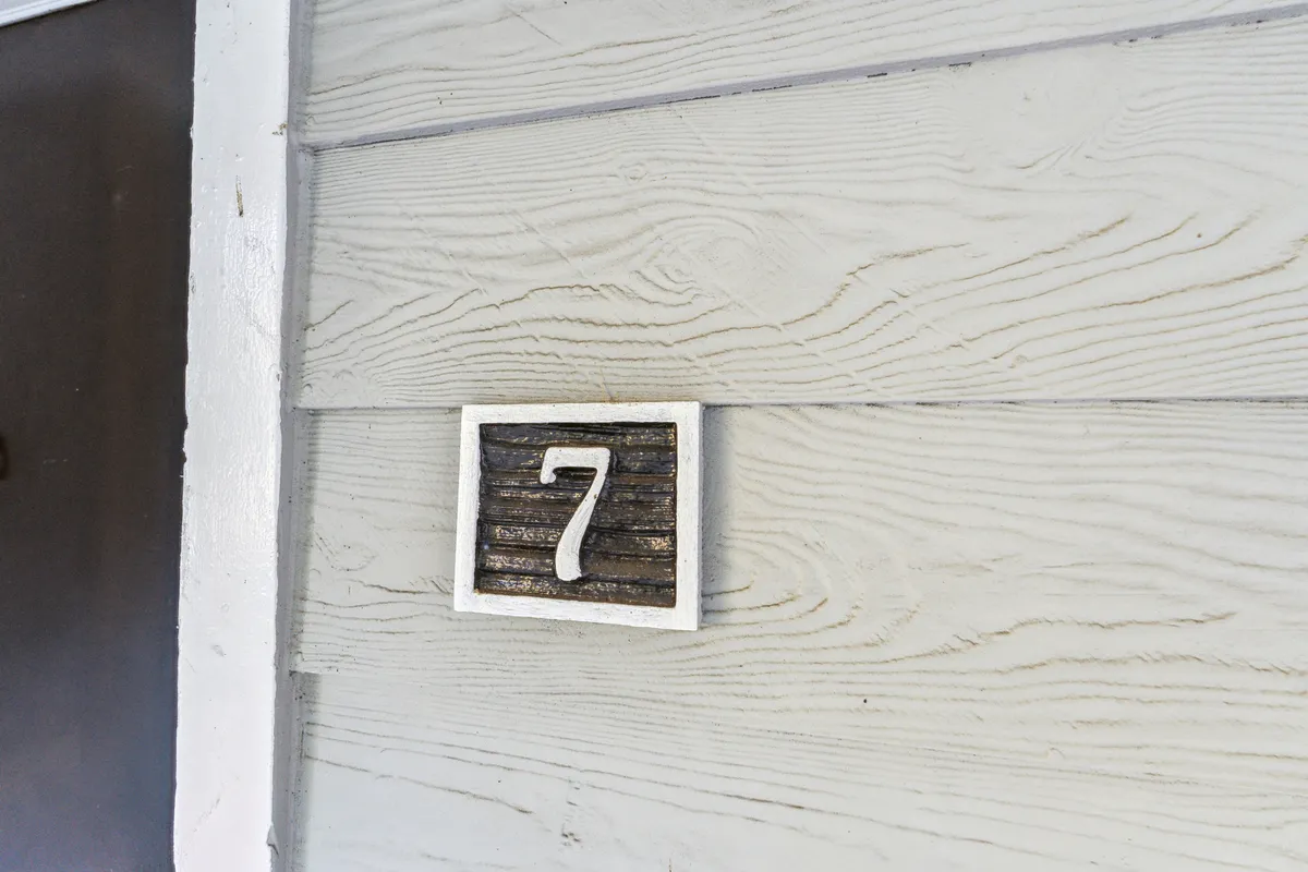 An inviting exterior view featuring a distinct house number '7' on a textured wall, hinting at the entrance to a residence. The image evokes the initial moment of arrival and a sense of belonging in a new place.