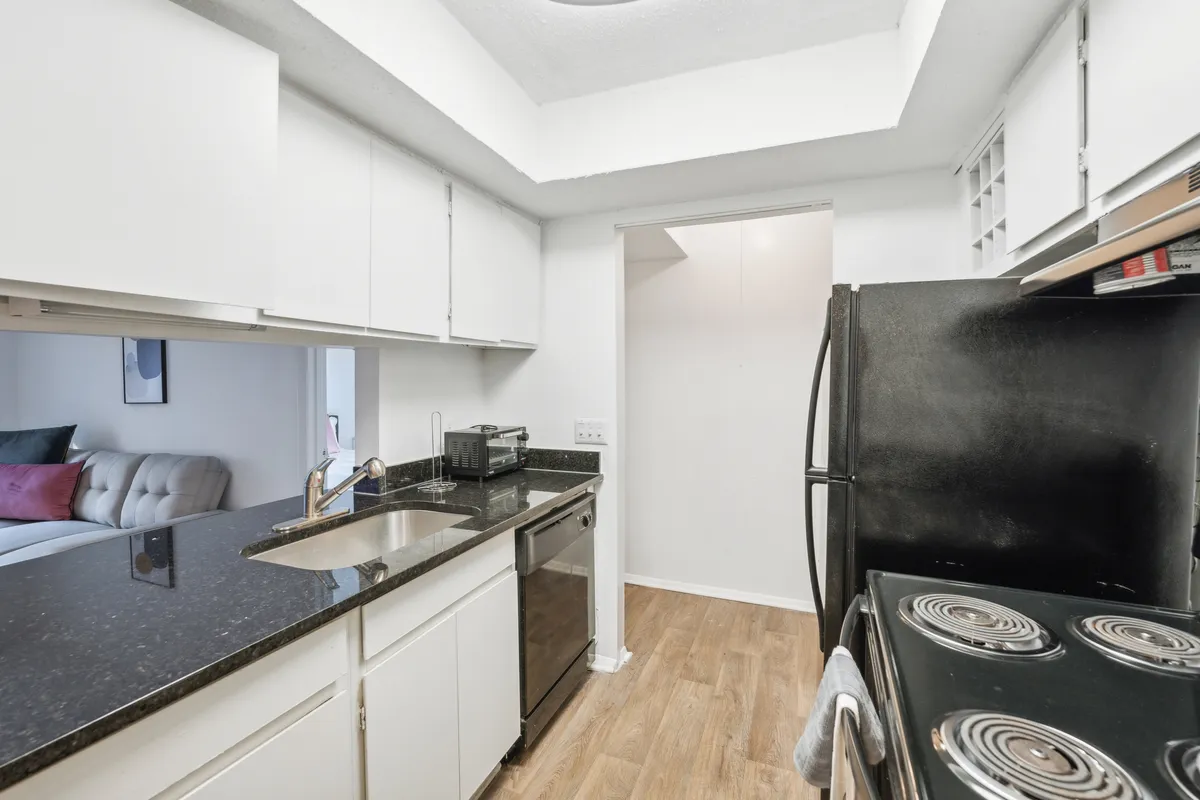 A bright, inviting kitchen with black appliances, a grand granite countertop, and white cabinets. The scene suggests an environment ideal for cooking, baking, and entertaining, with all essentials in easy reach.